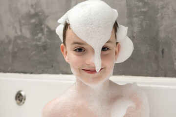 A happy child in a bathtub covered with fluffy foam, smiling playfully. Cute bath time moment, fun,...
