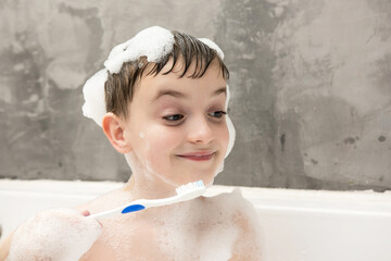 A young child enjoying a bath, with soap bubbles on their head and shoulders, looking down and...