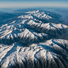 A breathtaking aerial view of snow-covered mountaintops against a pale blue sky.