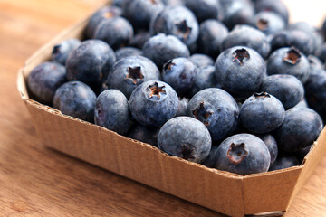 Fresh blueberries in eco-friendly cardboard box on wooden table. Natural organic fruits rich in antioxidants. Close-up. 