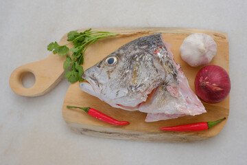 Raw golden snapper heads ready for cooking with some spices on wooden cutting board