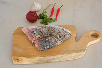 Raw golden snapper heads ready for cooking with some spices on wooden cutting board
