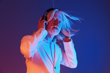 Elderly man with long hair listening to music in stylish attire against a vibrant blue and purple...