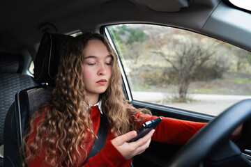A young woman looking at a mobile phone while driving a car. A female driver in the driver's seat...