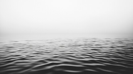 Naklejka premium Gentle ripples dance across a tranquil expanse of water, framed by a subtle mist that cloaks the distance. Early morning light casts a serene ambiance over the scene