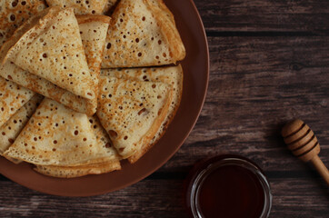 Baking openwork pancakes in a hole triangles on a plate on a dark background with honey