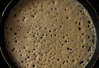 An openwork pancake is baked in a pan in a hole