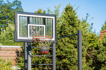 Basketball hoop with ball in outdoor setting surrounded by greenery on a sunny day