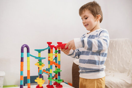 A 5-year-old boy plays with a multi-colored construction set, a labyrinth for balls. Development of logic and fine motor skills in preschool children. Independent play