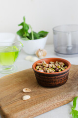 Peeled roasted pistachios in a ceramic bowl on a wooden board with ingredients. The process of making pistachio pesto. Vertical orientation. Selective focus.