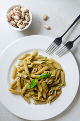 Penne pasta with pistachio pesto with a sprig of basil in a white plate with a fork on the table. Italian cuisine concept. Horizontal orientation. Selective focus. top view