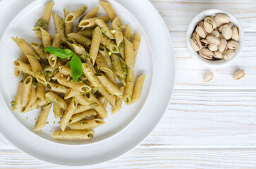Penne pasta with pistachio pesto with a sprig of basil in a white plate with a fork on the table. Italian cuisine concept. Horizontal orientation. Selective focus. Top view. Copy space