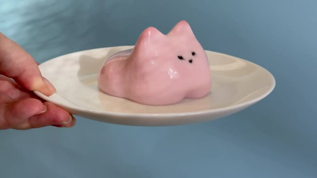 Italian dessert Panna Cotta in shape of cute cat, close up. Pink fruit panna cotta moves cool if you shake it