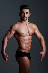 Slim muscular male model at black background. Fitness shirtless guy in posing in studio. Man with six pack abs. Brutal sexy man with six pack abs, fitness male model. Muscled guy.