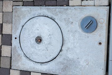 Stone manhole cover set in a paved surface. The cover is circular with a smaller round cap on the side.