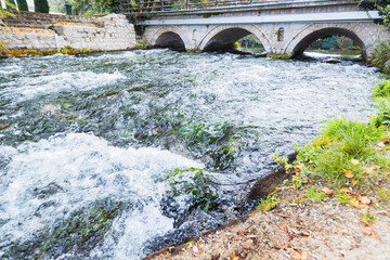 The Crni Drim River flows under a stone bridge with three arches, creating a picturesque scene as...
