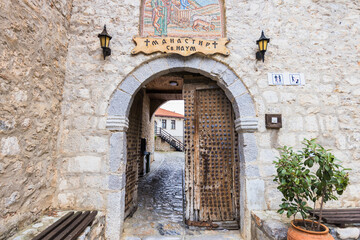 The arched stone entrance to St. Naum Monastery, featuring a large wooden door, a mosaic above, and...