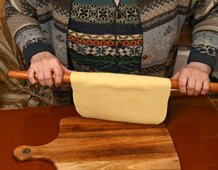 Homemade pasta preparation with a wooden rolling pin by a skilled cook in a cozy kitchen at midnight