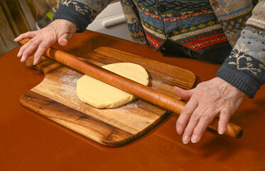 Woman rolls out dough on a wooden board in a warmly lit kitchen.