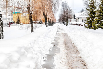 Obraz premium A snow-covered sidewalk with a clear walking path, leading into the distance, symbolizing the change of seasons..