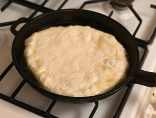 Dough rising in a cast iron skillet over a gas stove during meal preparation on a warm afternoon