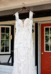 Close-up of a wedding dress hanging on a hanger in front of a house. Lace wedding dress hanging in front of house door outdoors on wedding day for bride, cropped photo