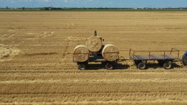 Above view on excavator as loading straw bales on trailer, tow by tractor at farmland, using forklift blade, additional carrier.