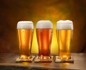 Three glasses of chilled beer on old wooden table and dark wall at the background.