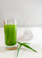 Aloe vera juice in glass with towel on a white table.