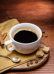 Cup of coffee on white plate, several coffee beans and brown sugar on wooden table close up. Top view.