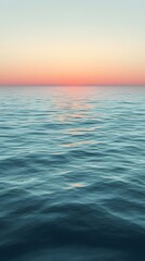 Obraz premium A serene view of the ocean at dusk, showcasing gentle waves reflecting soft hues of orange and pink as the sun sets on the horizon.