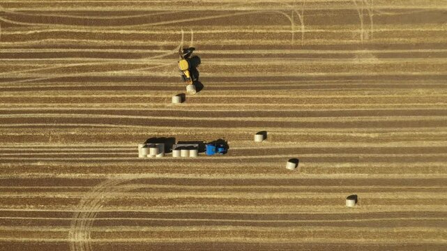 Above top view, dolly move follow the machines as they move to new position, excavator as loading straw bales on trailer, tow by tractor at farmland, using forklift blade, additional carrier.