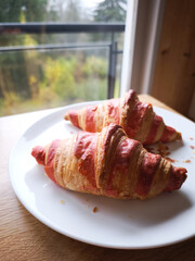 Two raspberry croissants sit on a white plate by a window overlooking a garden in chamonix, france, breakfast Valentines day