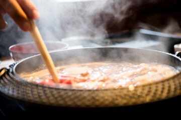 Holding sliced pork using chopsticks on hot pot with smoke for Japanese hot pot also known as Shabu Shabu or Sukiyaki is Japanese style.