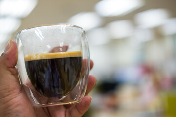 Man hand holding a double walled glass mug with black coffee in office