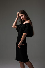 Elegant woman posing in a black dress against a neutral background while showcasing her long hair and poise
