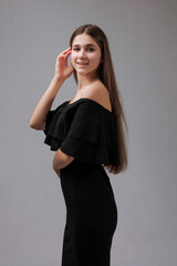 Young woman poses elegantly in a stylish black off-shoulder dress with a confident smile