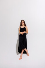 Fototapeta premium Elegant woman in a black dress poses against a minimalist white backdrop in a fashion studio setting
