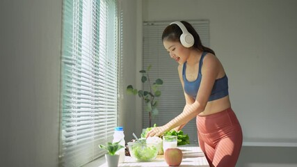 Woman wearing headphones, enjoying music, and preparing a fresh salad in a sunlit kitchen. She is focused and relaxed, creating a healthy meal with fresh ingredients