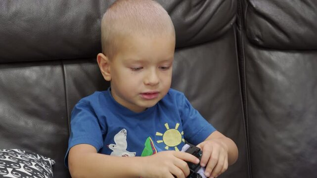 Child playing with new toy sitting on sofa at home. Concentrated face of little boy holding transformer robot toy. Three year old child examining new toy comments on his actions.