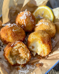 Golden Sicilian arancini with crispy coating and rich filling. Traditional Italian rice balls with cheese and meat stew, served with Parmesan and lemon on rustic craft paper. Vertical composition