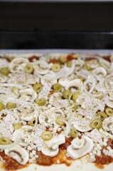 Vertical shot of an uncooked pizza with sliced olives and mushrooms