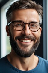 smiling man with glasses and beard in front of window