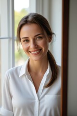 smiling woman in white shirt standing by window with white shirt
