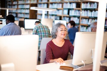 Elderly woman using a computer in a library. Focused senior working on a desktop. Learning and...