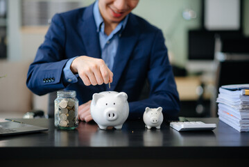 Smiling businessman saves money with piggy bank and coins; ideal for themes of finance, savings,...