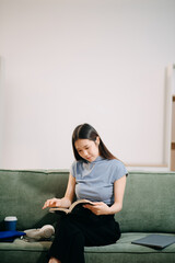 Obraz premium Young asian woman using smartphone and tablet while seated on couch at home