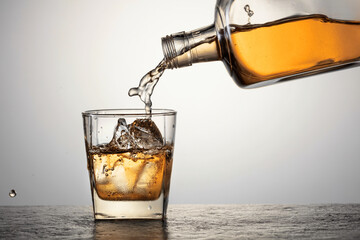 Whiskey is poured from a bottle into a glass with ice.