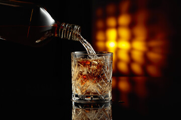 Pouring whiskey from a bottle into a glass with ice.