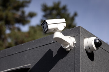 Surveillance camera CCTV. Close-up of modern surveillance cameras mounted on a dark building corner, ensuring security and monitoring, with a blurred tree background on a sunny day. Home security.
